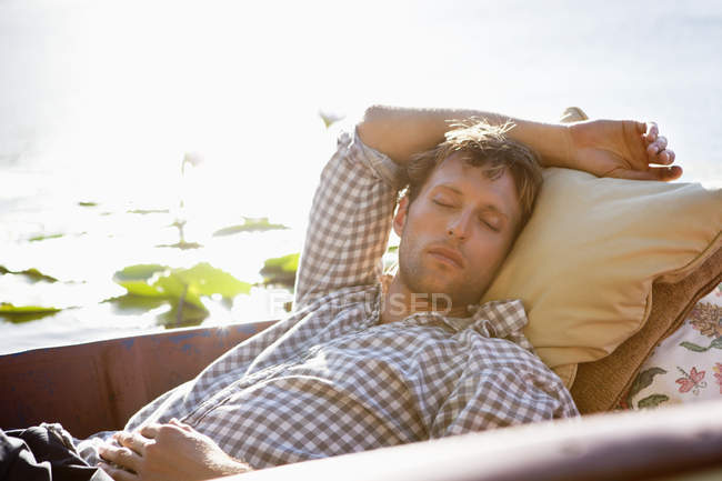 Relaxed young man sleeping in boat on lake in countryside — Stock Photo