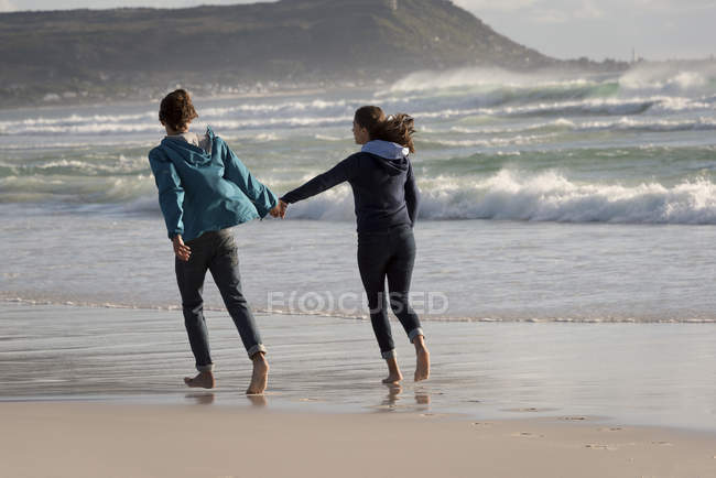 Щаслива молода пара біжить на пляжі тримає руки — стокове фото