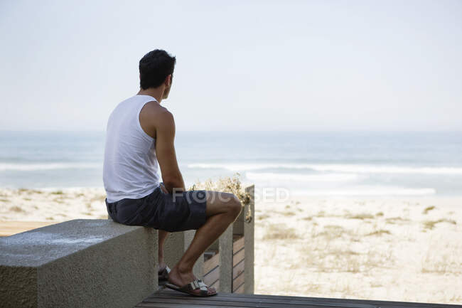 Vista trasera de un hombre sentado en un paseo marítimo - foto de stock