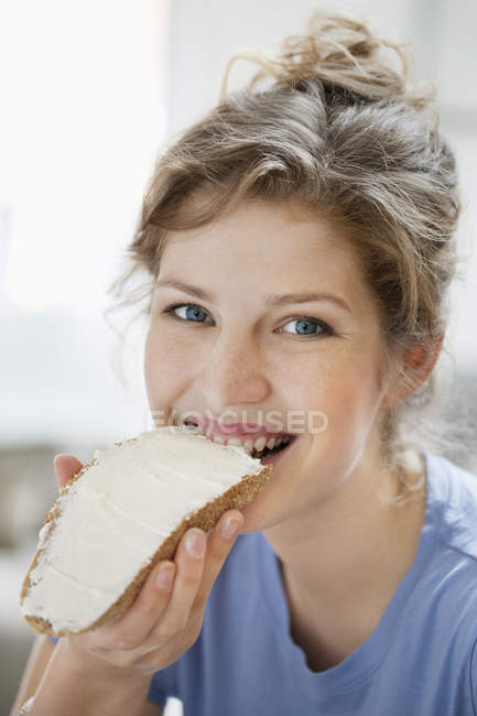 Retrato de mulher sorridente comendo torradas com creme de propagação — Fotografia de Stock