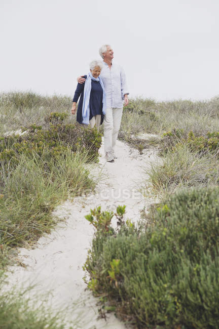 Счастливая старшая пара, идущая по тропинке на побережье — стоковое фото