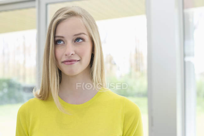 Close-up of blond woman smiling and looking away in front of window — Stock Photo