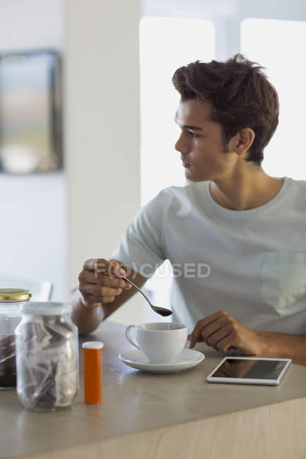 Молодий чоловік сидить за кухонним столом з чашкою кави — стокове фото