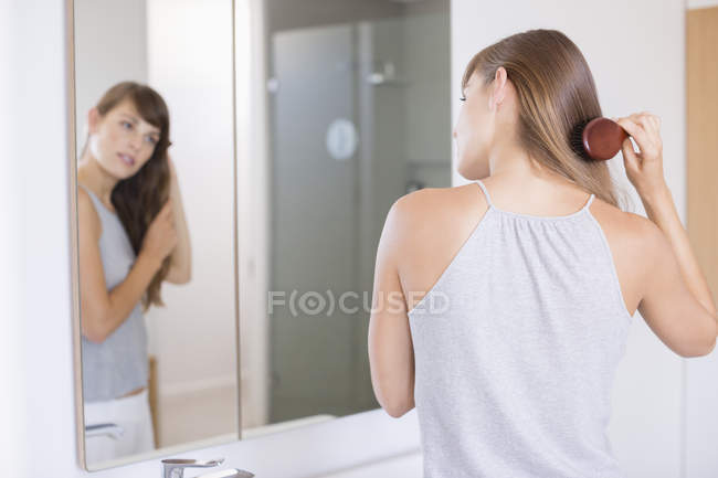 Woman combing hair in front of mirror in bathroom — Stock Photo