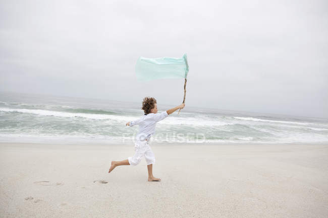 Boy running while holding flag on sandy beach — Stock Photo