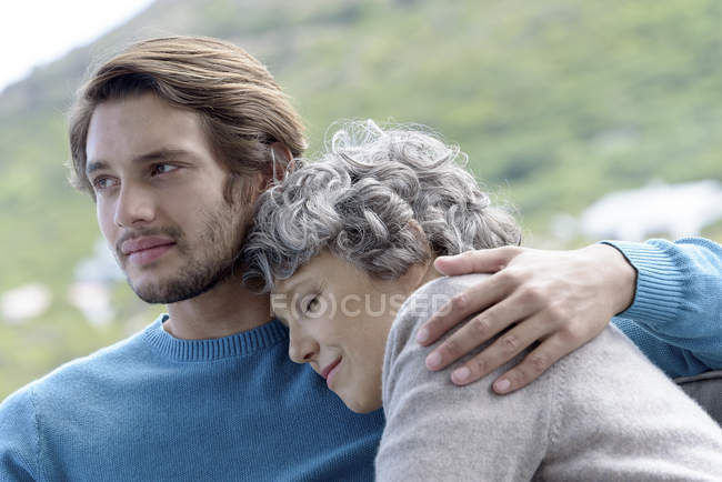 Loving son hugging relaxed mother outdoors — Stock Photo