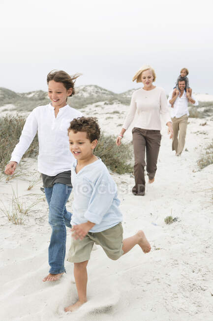 Pareja caminando por la playa con sus hijos - foto de stock