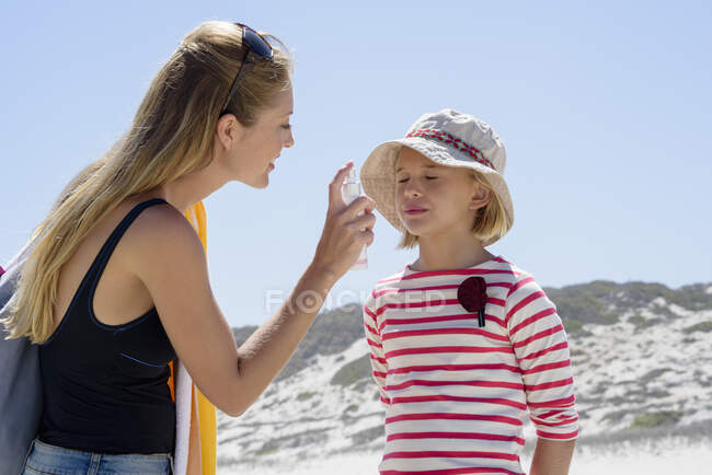 Madre aplicando protector solar a su hija en la playa - foto de stock