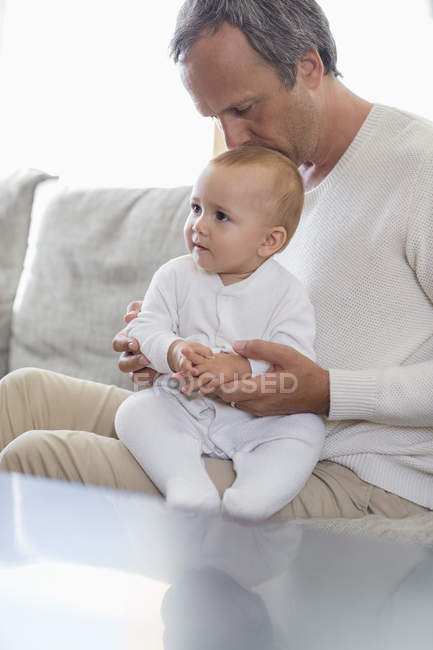Pai beijando bonito bebê filha no sofá na sala de estar — Fotografia de Stock