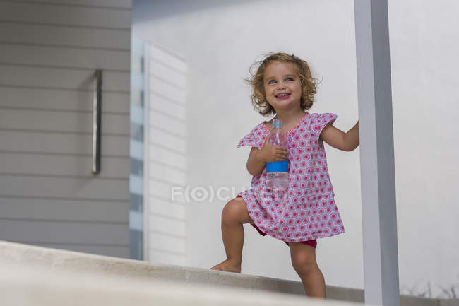 Happy baby girl holding water bottle on porch — Stock Photo