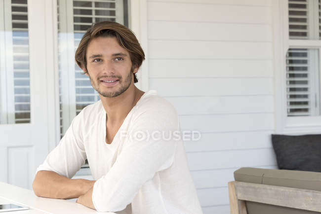 Счастливый молодой человек сидит на террасе и смотрит в сторону — стоковое фото