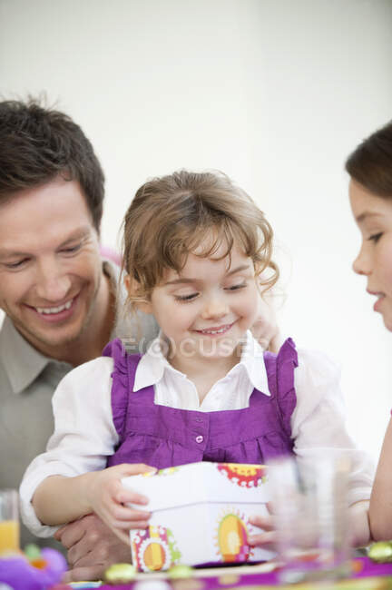 Girl opening her birthday present with her father and sister — Stock Photo