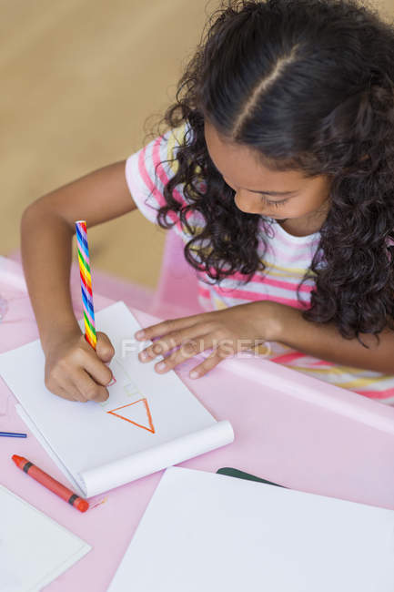 Зосереджена маленька дівчинка робить домашнє завдання за рожевим столом — стокове фото