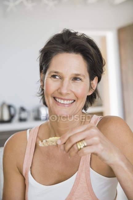Primer plano de la mujer sonriente comiendo en la cocina - foto de stock