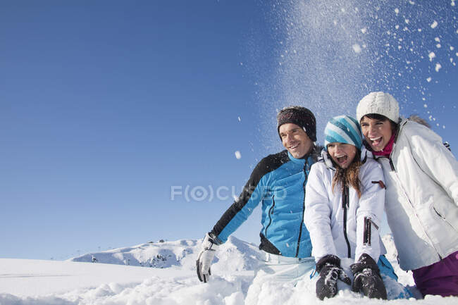 Pareja e hija en ropa de esquí, lanzando nieve al aire - foto de stock