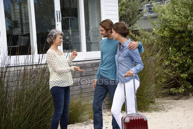 Happy mature woman meeting young couple with luggage outdoors — Stock Photo