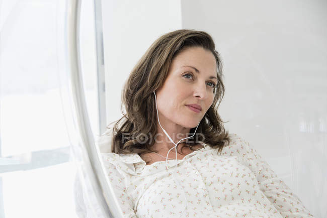 Mature woman listening to music in glass chair — Stock Photo