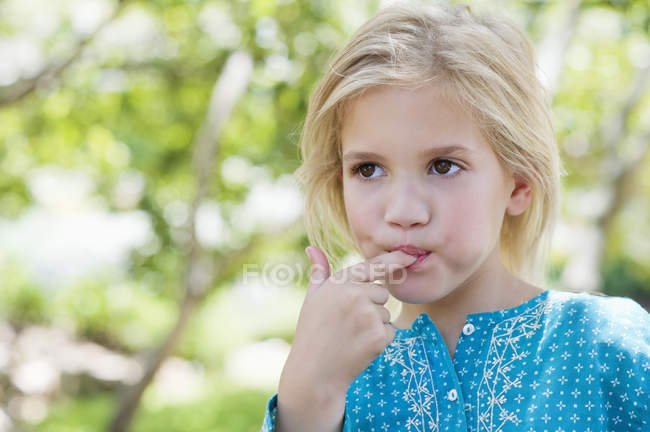 Primer plano de linda niña lamiendo el dedo al aire libre - foto de stock
