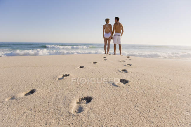 Footprints on sandy beach with couple standing on background and looking at view — Stock Photo