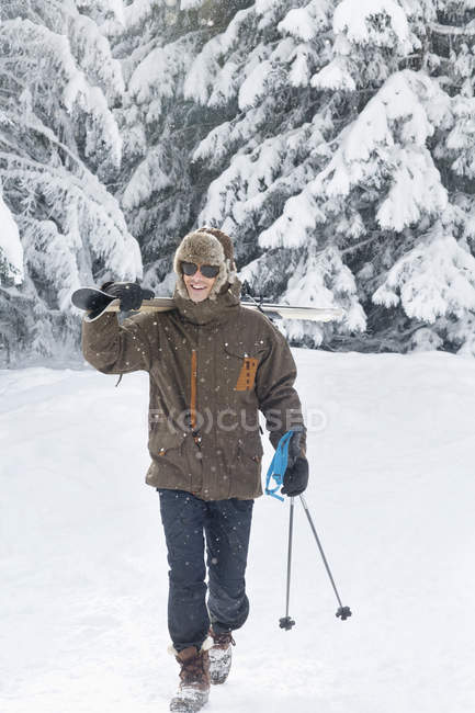 Jovem carregando esquis nos ombros na floresta de inverno — Fotografia de Stock