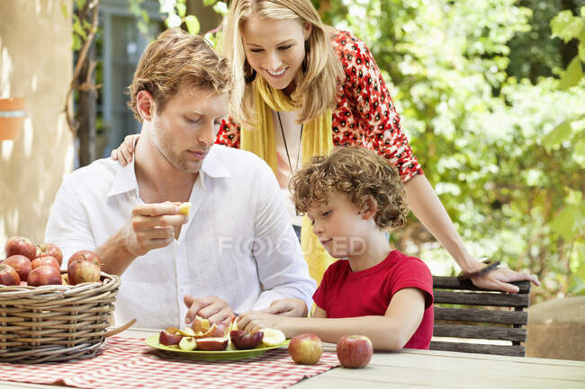 Madre y padre viendo a su hijo cortar manzanas - foto de stock