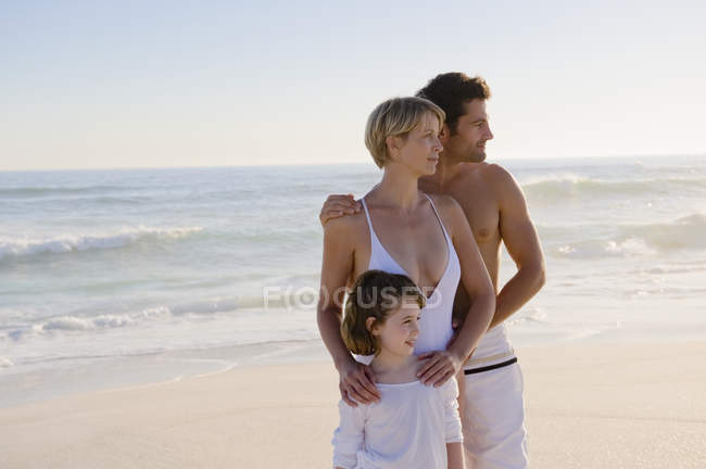 Happy thoughtful family standing on sandy beach — Stock Photo