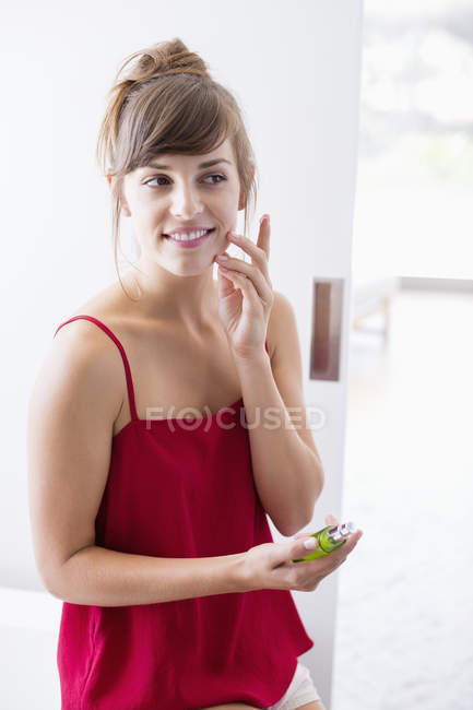 Junge Frau trägt Feuchtigkeitscreme auf Gesicht im Badezimmer auf — Stockfoto