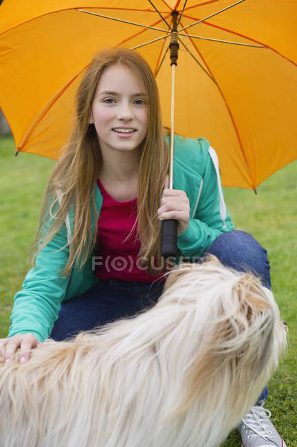 Portrait of teenage girl with umbrella pampering dog outdoors — Stock Photo