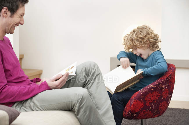 Alegre hombre e hijo leyendo libros en casa - foto de stock
