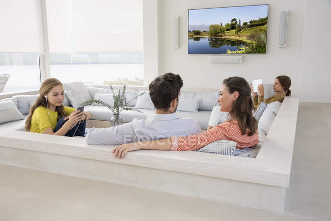 Coppia guardare la televisione con le figlie occupato con gadget — Foto stock