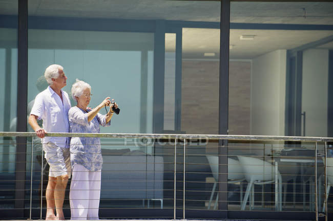 Mujer mayor tomando fotos con cámara digital mientras su marido mira hacia otro lado - foto de stock