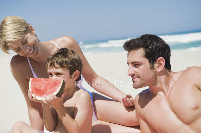Family enjoying watermelon on sandy beach — Stock Photo