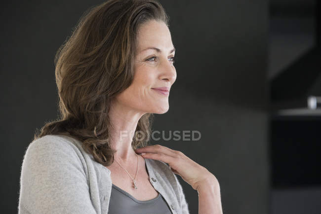 Smiling mature woman with brown hair standing on dark background — Stock Photo