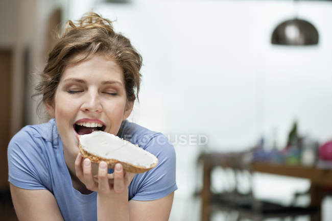 Portrait of young woman eating toast with cream spread — Stock Photo