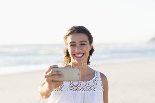 Jeune femme prenant selfie avec smartphone sur la plage — Photo de stock