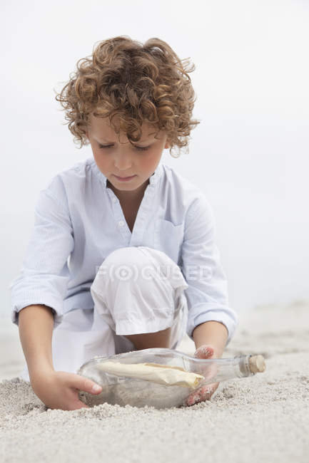 Cute boy looking at message in a bottle on sandy beach — Stock Photo