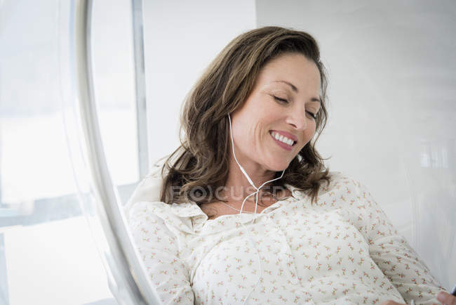 Mulher madura ouvindo música em cadeira de vidro — Fotografia de Stock