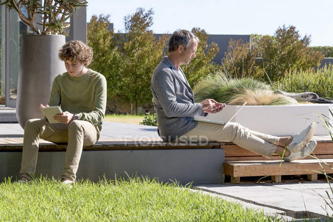 Щасливий батько і син використовують електронні гаджети в саду — стокове фото