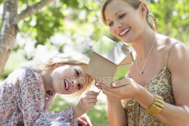 Little girl and her mother looking at dollhouse outdoors — Stock Photo