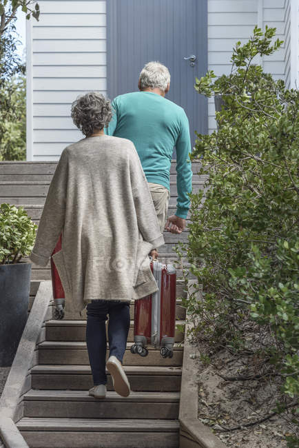 Seniorenpaar trägt Koffer auf Treppe vor Haus — Stockfoto