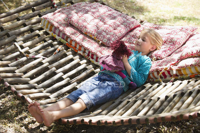Bambina che gioca con il giocattolo mentre si trova in amaca nel giardino estivo — Foto stock
