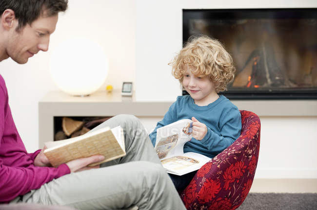 Homem e filho lendo livros em casa — Fotografia de Stock