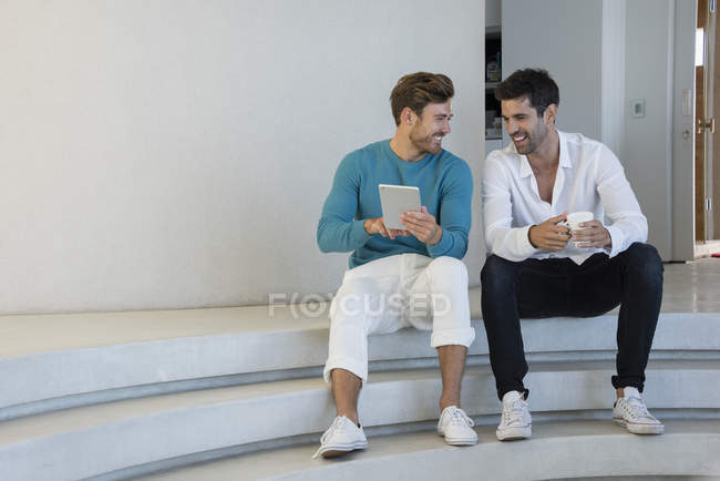 Amigos varones felices usando tableta digital en escaleras - foto de stock
