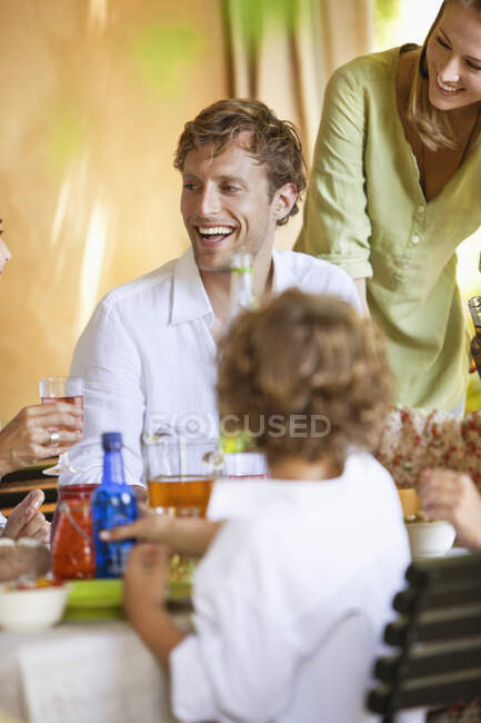 Familia tomando bebidas y discutiendo en la mesa de comedor - foto de stock
