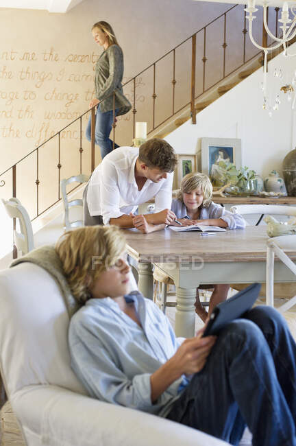 Мужчина разговаривает с маленьким мальчиком с братом, используя цифровой планшет на переднем плане в доме — стоковое фото