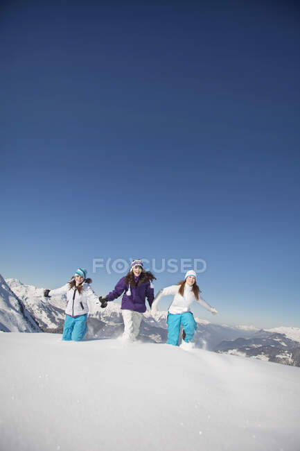 Tres chicas adolescentes en ropa de esquí, corriendo en la nieve - foto de stock