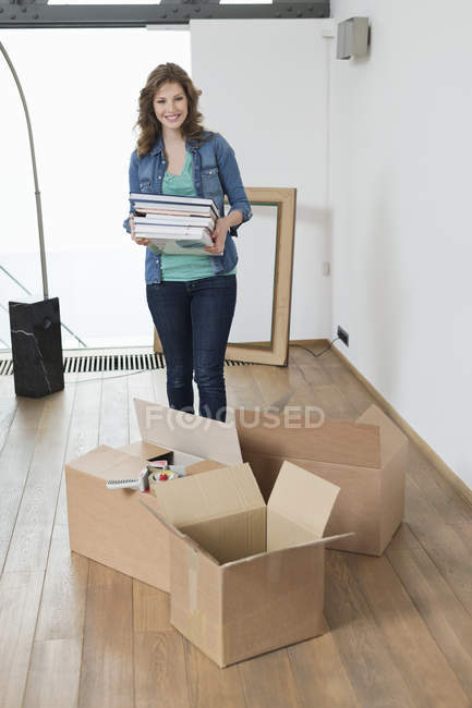 Mujer llevando pila de revistas en apartamento con cajas de cartón - foto de stock
