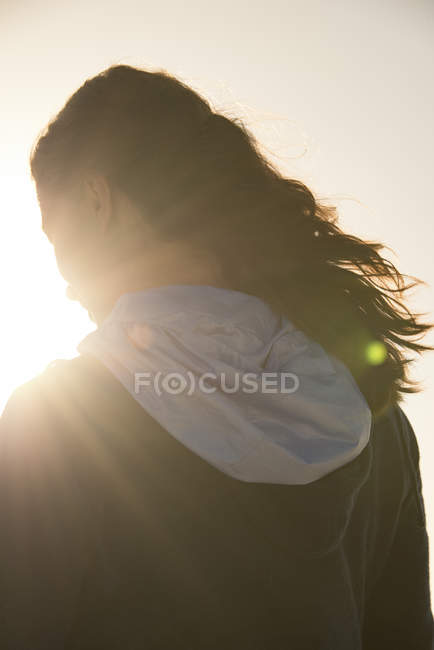 Visão traseira da jovem mulher com capuz em pé à luz do sol — Fotografia de Stock
