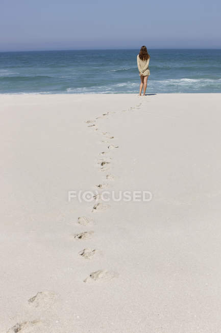 Вид сзади расслабленной женщины, стоящей на песчаном пляже — стоковое фото
