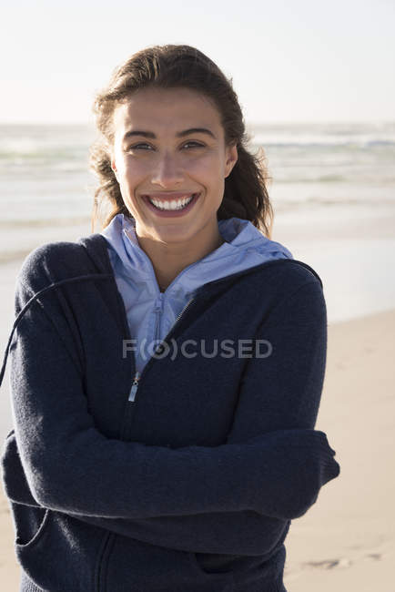 Portrait of young charming woman in warm hoodie standing on beach — Stock Photo